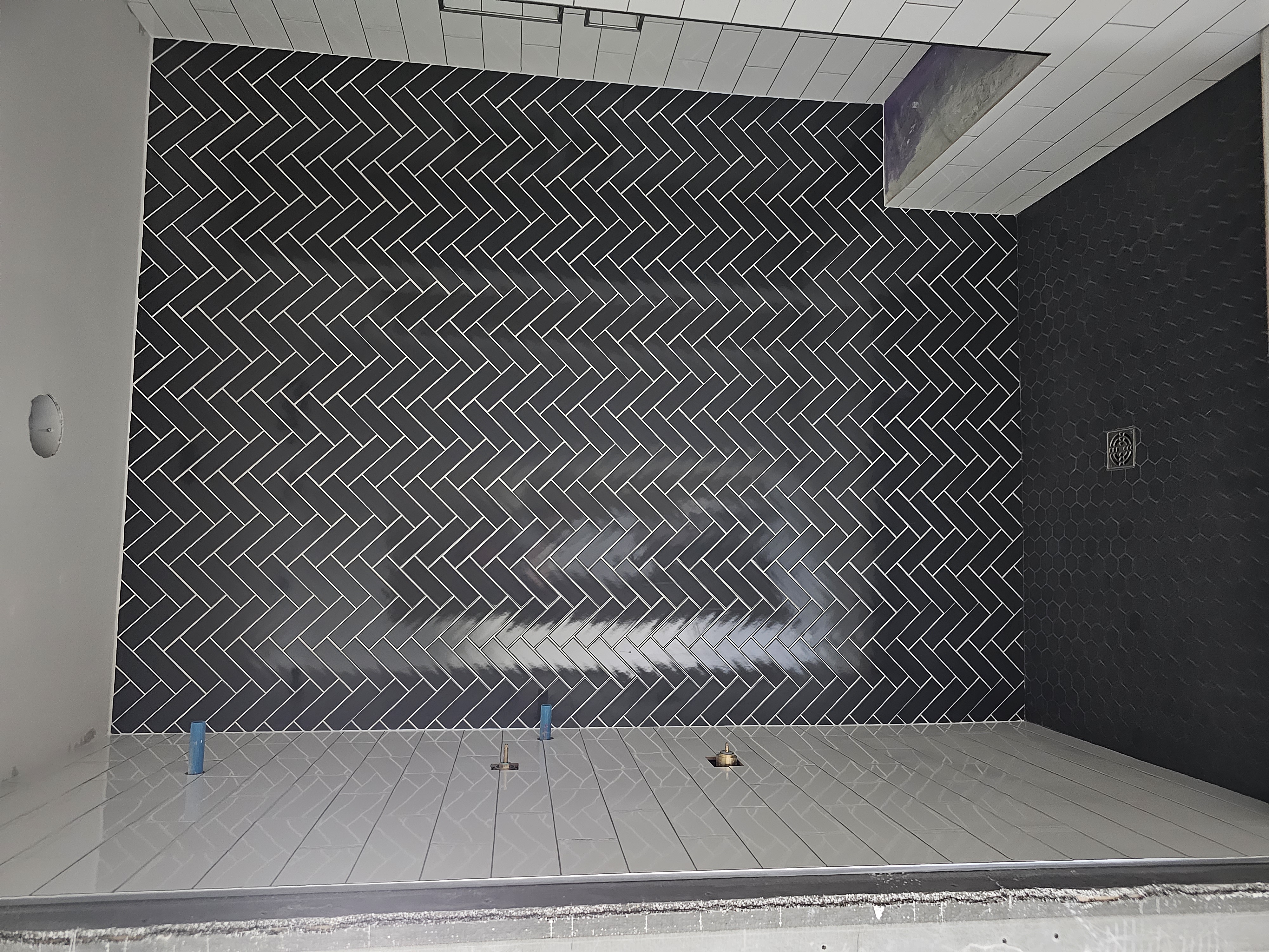 Walk-in shower with glossy black herringbone accent wall and white subway walls