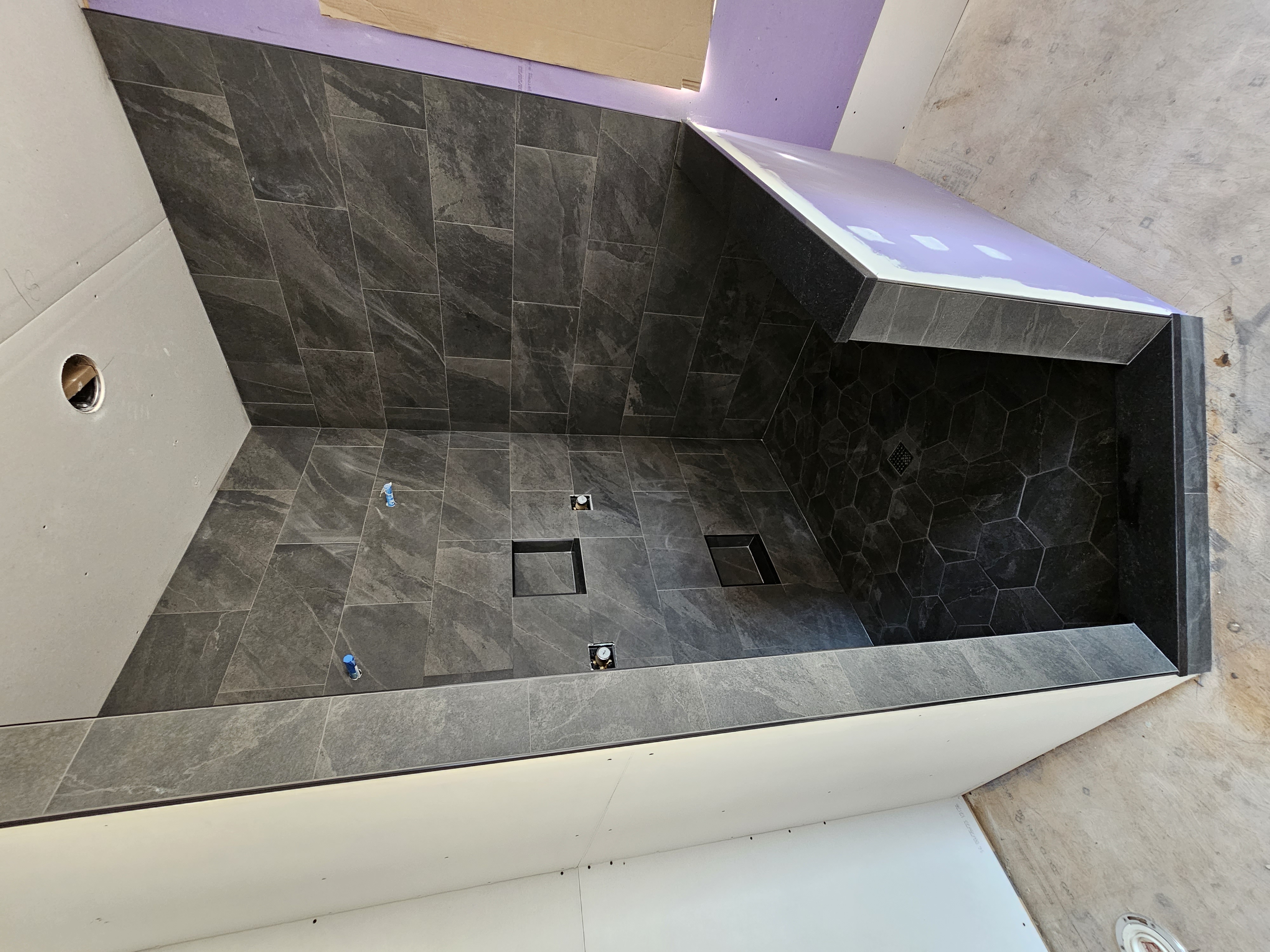 Charcoal large-format walk-in shower with dark hex floor and slab pony wall