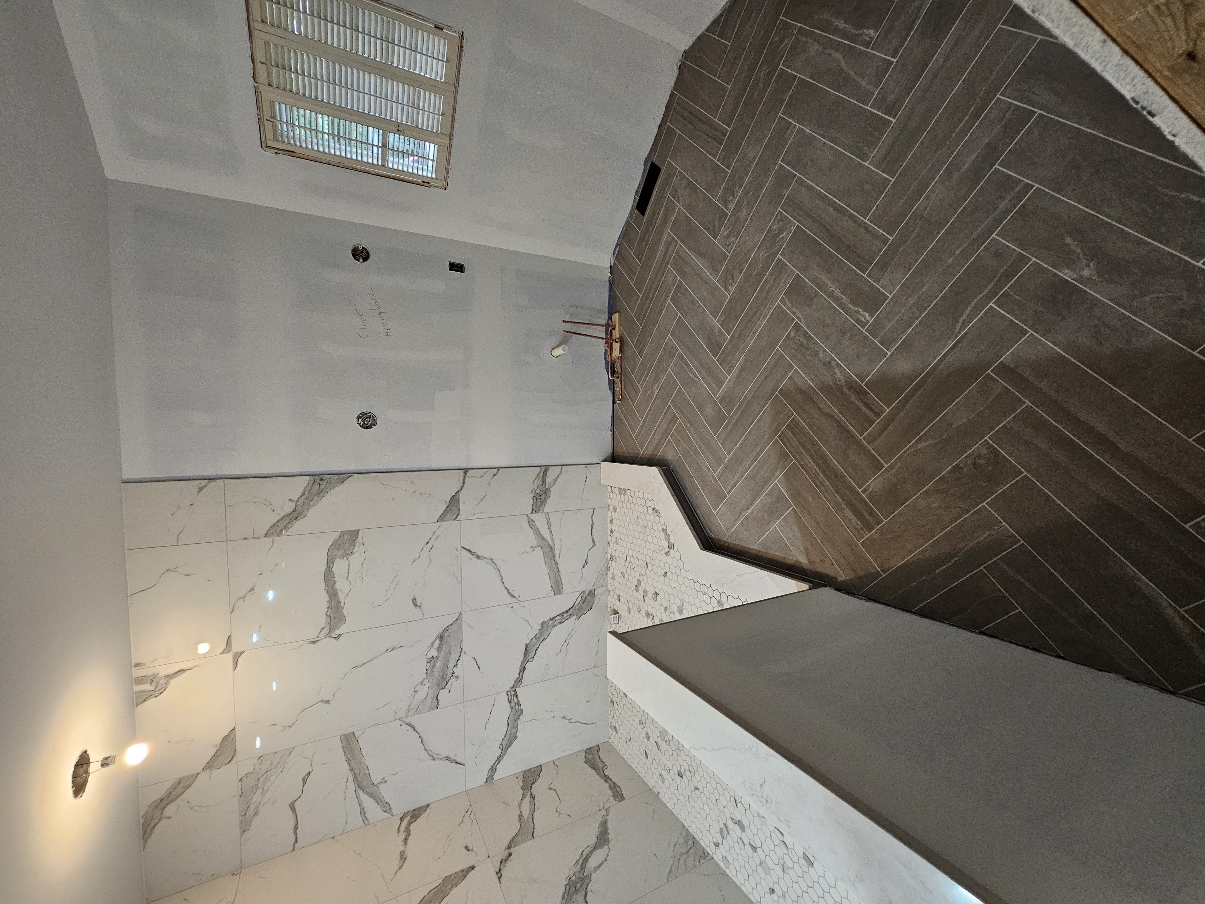 Walk-in wet room with marble-look walls, hex shower floor, and dark herringbone main floor