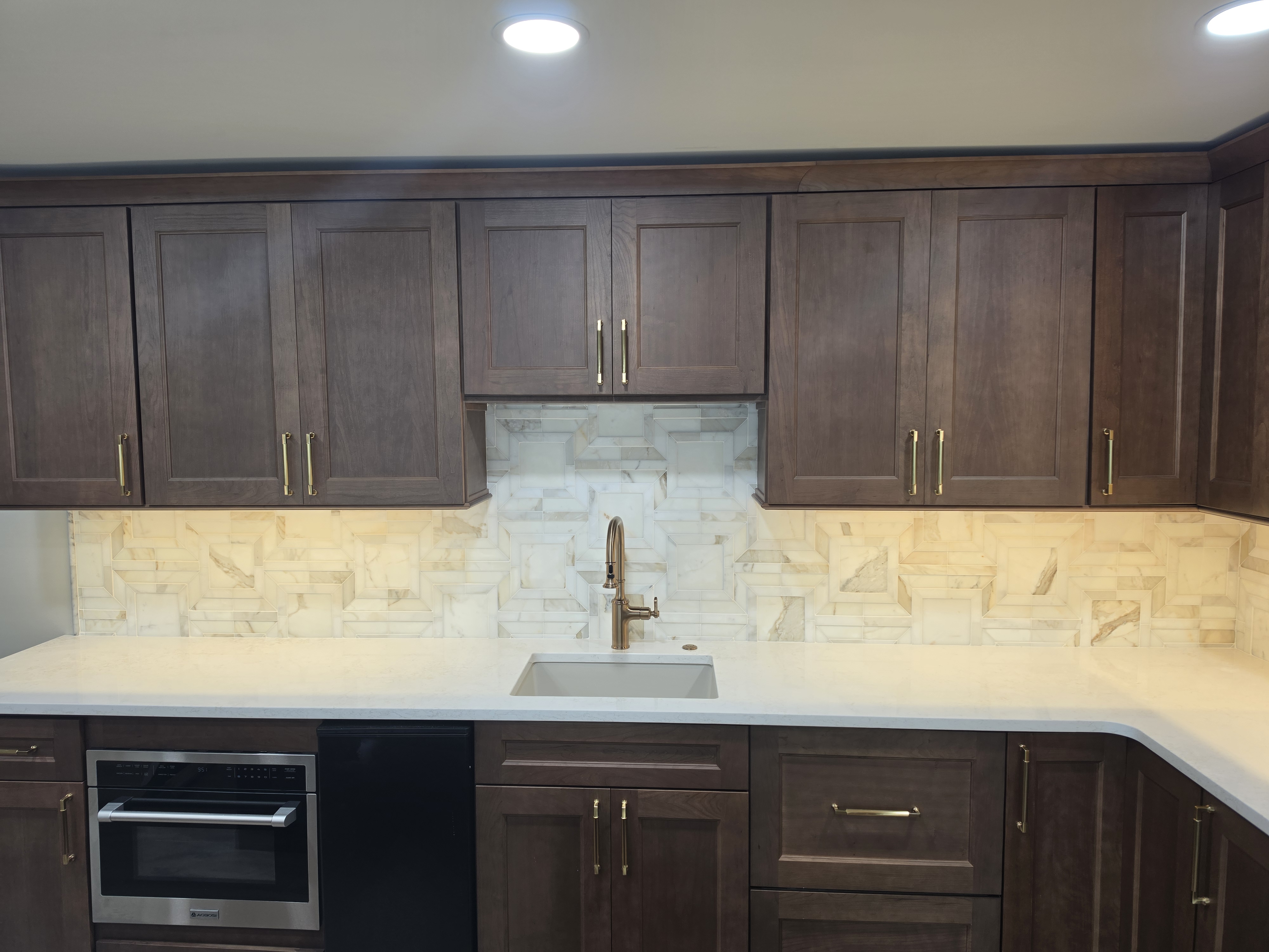 Kitchen marble geometric backsplash with dark cabinets and brass faucet